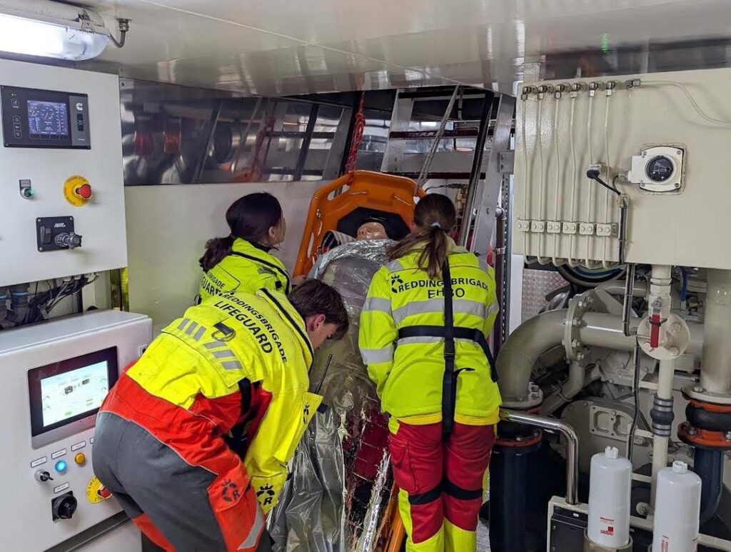 De lifeguards vervoeren slachtoffer op brancard vanuit machinekamer naar dek binnenvaartschip.
